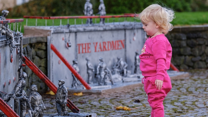 A young girl looks at The Yardmen sculptures by Jason Orr; a series of 12" tall, silver effect metal figures depicting scenes from Greenock's shipbuilding past. One of the small figures appears to be staring back at her.
