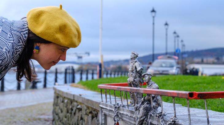 A woman wearing a yellow beret stares at one of the figures within Jason Orr's Yardsman sculptures at Greenock Waterfront.