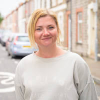 Claire, standing in her street smiling