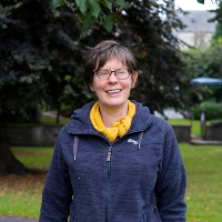 Felicity stood in a leafy green park, smiling and wearing a zip-up outdoor fleece top.