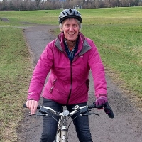 Karen Wilson smiling as she cycles on her bicycle through a park in Edinburgh