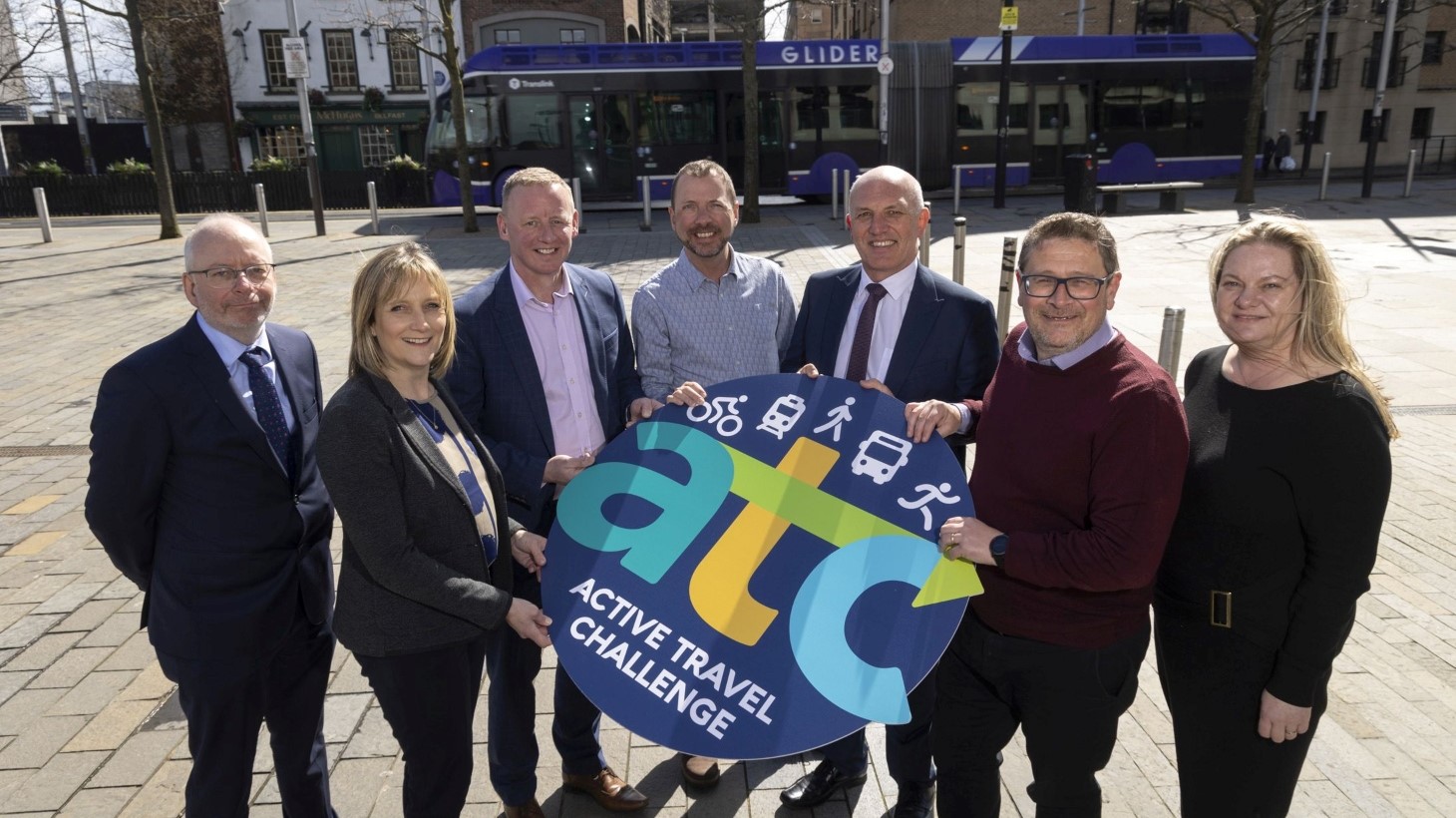 A group of women and men stand together holding a round sign saying 'A-T-C' for the launch of the 2024 Active Travel Challenge.