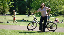 Woman outside in sunshine in a park with an ebike 